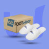 Hotelausstattung von GC Footwear: Ein Paar weiße Frottee-Slipper mit gesticktem Logo neben einem passenden Lieferkarton.