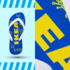 Ein einzelner blauer Flip-Flop mit weißen Riemen, der auf einem hellblauen Hintergrund schwebt. Die Sohle ist mit gelben Linien bedruckt, die verschiedene Möbelstücke zeigen. In der Mitte steht in großen, gelben Buchstaben „IKEA“. Im oberen rechten Bildausschnitt ist eine vergrößerte Ansicht des „IKEA“-Schriftzugs zu sehen.