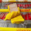 Ein Paar gelbe Socken mit rotem "NN"-Muster und dem Schriftzug "Netto" liegt auf einem Einkaufswagen. Daneben ist eine Karte mit der Aufschrift "Dann geh doch mit Netto!" zu sehen.