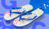 Ein Paar weiße Flip-Flops mit blauen Riemen und einem bunten "STEAM"-Logo auf der Sohle. Die Flip-Flops liegen auf einem zweifarbigen, blauen Hintergrund.