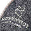 Nahaufnahme eines grauen, filzartigen Materials mit dem weiß gestickten Logo "HUSSNHOF FARM LODGE".