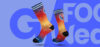 Ein Paar Socken mit einem Farbverlauf von Rot zu Blau, auf denen das Logo "#WRMNGHS" zu sehen ist, vor einem blauen Hintergrund mit dem weißen Schriftzug "GOOD WEEK".
