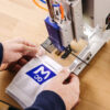 Ein Arbeiter platziert eine weiße Socke mit einem blauen Logo in einer Maschine, die ein kleines schwarzes Logo auf der Socke anbringt.