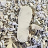 Eine fertige Schuhsohle liegt auf einem Haufen aus recyceltem Kunststoffgranulat, um die nachhaltige Produktion zu symbolisieren.