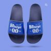 Eine dunkelblaue Badeschlappe, die auf einem violett-blauen Hintergrund schwebt. Die Schuhbrücke ist dunkelblau und zeigt ein weißes geprägtes Motiv mit der Aufschrift „Bitburger 0.0 % vol.“ und „bitte ein bit“.