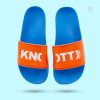 Ein Paar blaue Badeschlappen mit orangefarbenem Riemen, die auf einem hellblauen Hintergrund schweben. Der Riemen trägt in weißen Großbuchstaben die Aufschrift „KNOTT“. Ein vergrößerter Ausschnitt des Riemens ist im oberen rechten Bildausschnitt zu sehen.