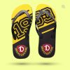 Ein Paar Flip-Flops auf einem hellen gelben Hintergrund. Die Sohlen sind gelb mit großen umrandeten Zahlen "1953" über beide Sohlen, bedruckt. Unten auf der Ferse ist das "Dynamo Dresden" Logo zu sehen. Der Flip-Flop hat schwarze glatte glänzende Riemen