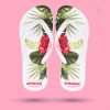 Ein Paar weiße Flip-Flops, die auf einem pinken Hintergrund schweben. Die Sohlen sind mit einem Muster aus großen, roten Hibiskusblüten und grünen Blättern bedruckt. Am unteren Rand steht in roter Schrift „ATTENSAM“.