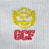 Eine Nahaufnahme von einer weißen Socke mit einem gestickten Logo, das einen Schnurrbart und Lorbeerblätter in Gelb sowie den roten Schriftzug "GCF" zeigt.