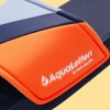 in Bildausschnitt, der eine Badelatsche zeigt. Der Riemen ist in den Farben Dunkelblau, blaugrau und Orange gehalten und hat eine erhabene Prägung mit dem weißen Schriftzug "AquaLetters" und einem kleinen Logo auf der Seite. Das Fußbett der Sandale ist navy blau. Der Hintergrund ist beige.