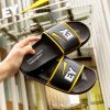 Verschiedene Badelatschen und Badeschuhe sind auf einem gelben Hintergrund mit dem Logo "GC FOOTwear" ausgestellt. Zu sehen sind unter anderem Badelatschen von Hela, Knott, Bayer Leverkusen, NFT und West.