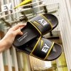 Verschiedene Badelatschen und Badeschuhe sind auf einem gelben Hintergrund mit dem Logo "GC FOOTwear" ausgestellt. Zu sehen sind unter anderem Badelatschen von Hela, Knott, Bayer Leverkusen, NFT und West.