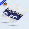 Weiße Badelatsche mit einem Riemen, der mit einem blau-schwarzen Muster und großen, weißen Buchstaben bedruckt ist, im Branding der Firma GC Footwear. Oben links im Bild ist ein "48 h express" mit "Made in Germany" badge angezeigt.