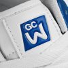 Eine Detailaufnahme eines blau weiß Geprägten Logos auf einer weißen Lasche, auf der Schuhzunge eines weißen Sneakers mit blauen Einsätzen.