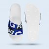 Eine Draufsicht auf weißen Badelatschen mit einer Schuhbrücke, die mit einem blau-schwarzen Muster und großen, weißen Buchstaben bedruckt ist, im Branding der Firma GC Footwear. Auf der rechten Seite ist die Sohle von unten zu sehen.