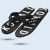 A pair of black flip-flops with the word “KOWALD” printed in large white letters on the sole. The straps are made of black technical fabric with a white diamond pattern.