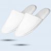 A pair of white hotel slippers shown at a side angle with plush material.